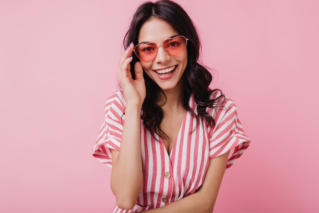 Mulher caucasiana alegre com um lindo sorriso tocando seus óculos. retrato de menina morena engraçada isolada.