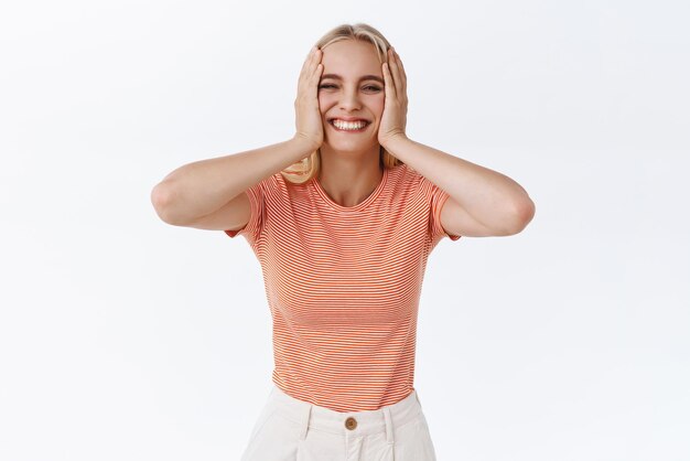 Mulher caucasiana bonita boba despreocupada em camiseta listrada com tatuagens aperta as bochechas e sorrindo alegremente parece satisfeita e alegre se divertindo sendo feliz aproveite a vida fundo branco