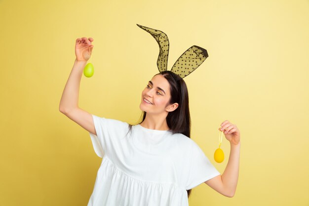 Mulher caucasiana como um coelhinho da Páscoa em fundo amarelo studio. Saudações de Páscoa feliz.