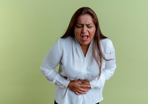 Mulher caucasiana de meia-idade, doente, casual, agarrada à mão dolorida na barriga isolada na parede verde