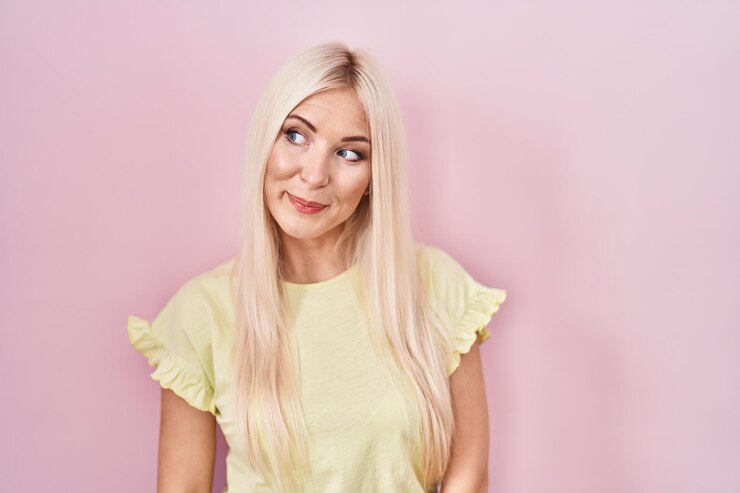 Foto grátis mulher caucasiana em pé sobre fundo rosa sorrindo olhando para o lado e olhando para longe pensando