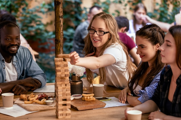 Mulher caucasiana está colocando um tijolo em uma torre alta no jogo de mesa jenga no restaurante