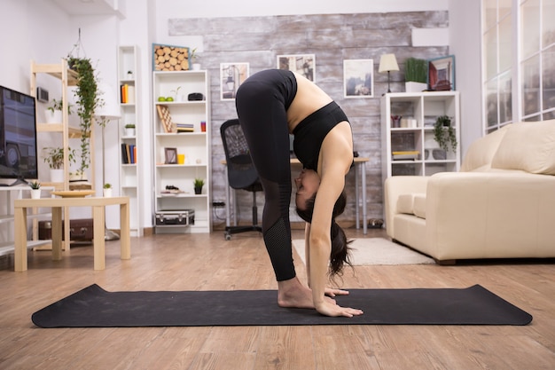 Mulher caucasiana, fazendo pose de ioga de flexibilidade na esteira na sala de estar. Estilo de vida pacífico.