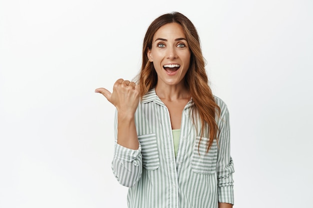 Mulher caucasiana impressionada apontando para a esquerda, sorrindo animada e olhando para a frente