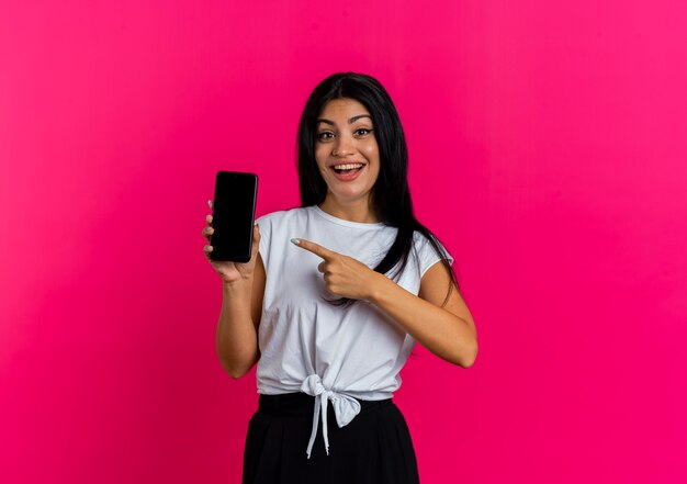 Mulher caucasiana jovem e alegre segurando e apontando para o telefone