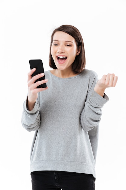 Mulher caucasiana jovem feliz conversando por telefone faz gesto de vencedor.