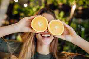 Foto grátis mulher caucasiana jovem feliz segurando laranjas frescas na frente dos olhos e sorrindo