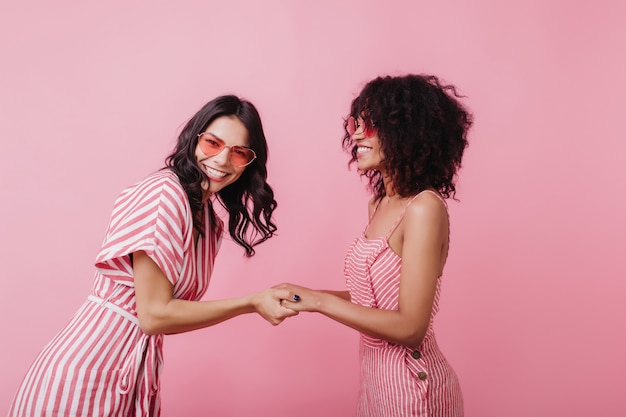 Foto grátis mulher caucasiana morena engraçada posando de brincadeira com a amiga. tiro interno de entusiasmada garota africana se divertindo.