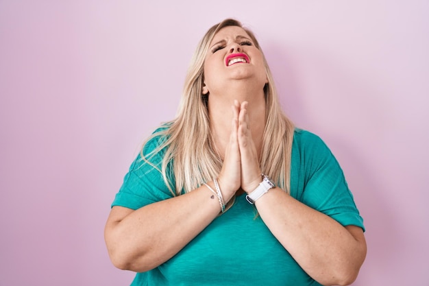 Foto grátis mulher caucasiana plus size em pé sobre fundo rosa implorando e rezando com as mãos junto com a expressão de esperança no rosto muito emocionada e preocupada implorando