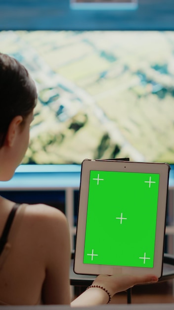 Foto grátis mulher caucasiana, segurando a tela verde verticalmente no tablet digital, olhando para o modelo de chroma key e fundo virtual de maquete isolado. jovem com equipamento moderno de espaço de cópia