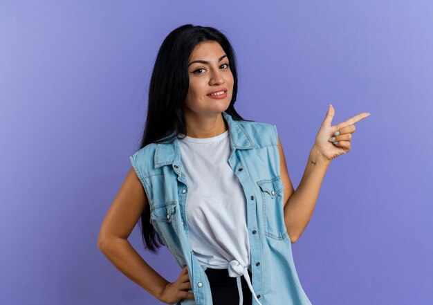 Mulher caucasiana sorridente apontando para o lado isolado em um fundo roxo com espaço de cópia