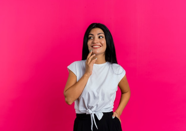 Mulher caucasiana sorridente coloca a mão no queixo olhando para o lado