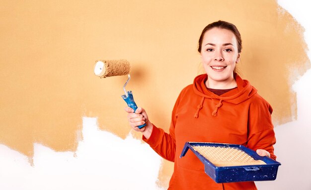 Mulher caucasiana sorridente pintando a parede interior de casa. apartamento em reforma. conceito de reparação e redecoração. espaço de cópia