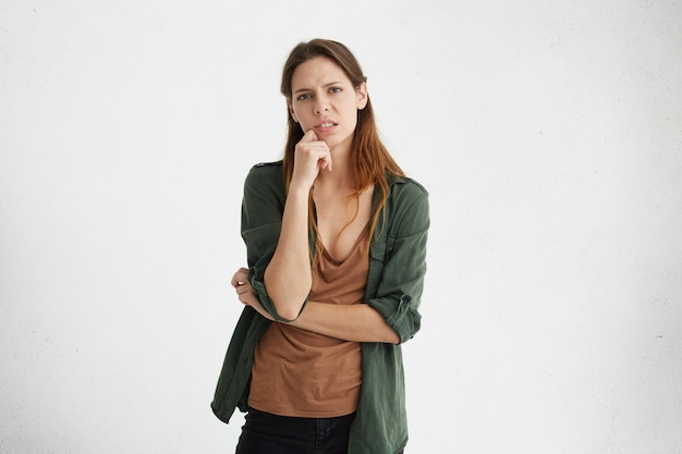 Foto grátis mulher chateada com bela aparência vestindo camiseta marrom casual e jaqueta verde, segurando a mão no queixo, com aparência cansada e infeliz.