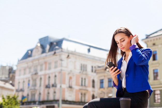 Mulher checa seu telefone sentado com uma xícara de café na rua