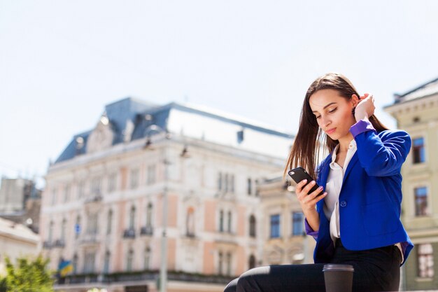 Mulher checa seu telefone sentado com uma xícara de café na rua