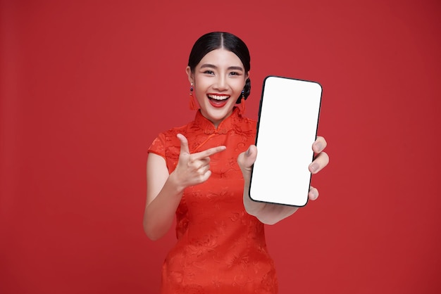 Mulher chinesa asiática feliz segurando um modelo de smartphone e apontando o dedo para uma tela em branco e sorrindo