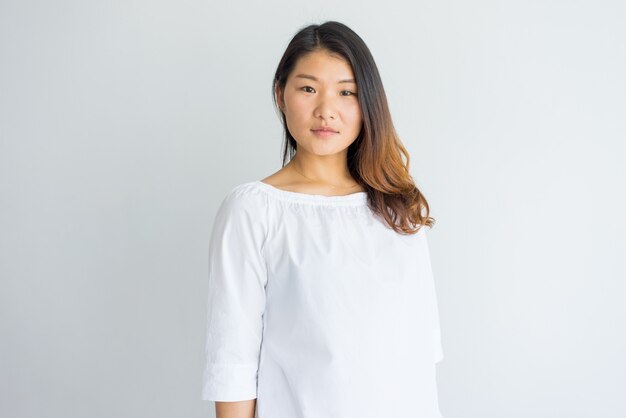 Mulher chinesa nova bonita séria na blusa branca que olha a câmera.