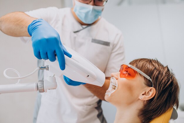 Mulher clareando dentes em odontologia com equipamentos especiais