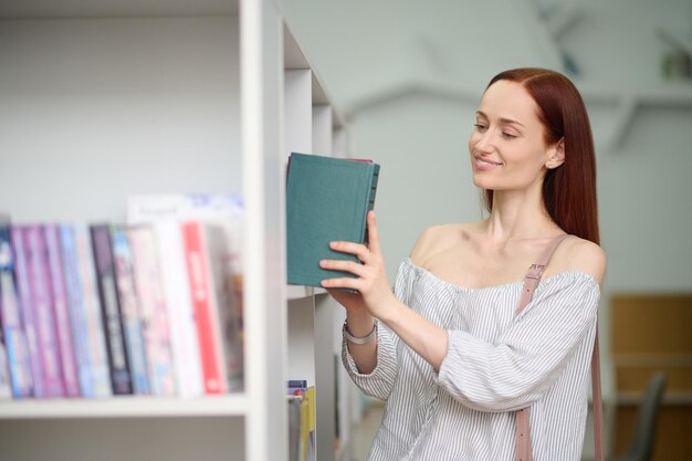 Mulher colocando livro na estante da biblioteca