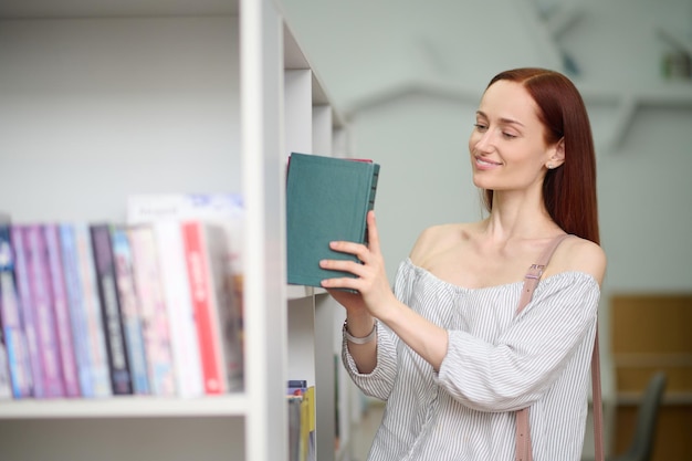 Mulher colocando livro na estante da biblioteca