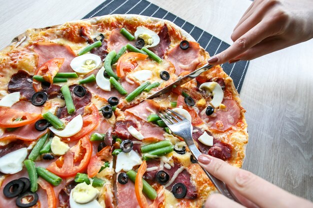Mulher com as mãos cortando pizza fresca com feijão, queijo, presunto, ovos, calabresa e legumes. cortando pizza