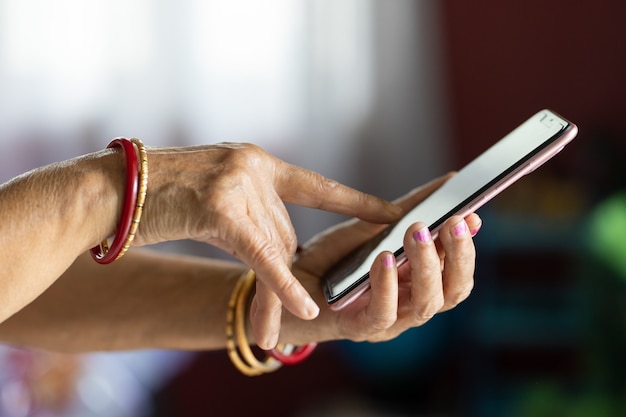 Mulher com as mãos enrugadas usando um smartphone com um fundo desfocado