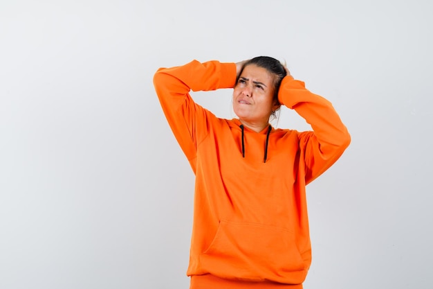 mulher com as mãos na cabeça com um capuz laranja e parecendo esquecida