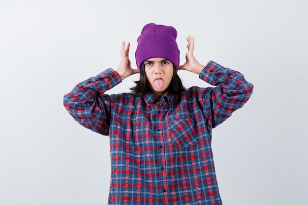 Mulher com as mãos na cabeça com uma camisa quadriculada e um gorro parecendo engraçada