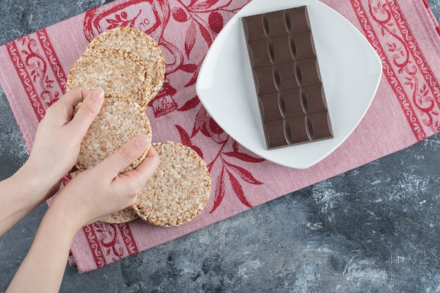 Mulher com as mãos segurando um pão de arroz crocante com barra de chocolate.