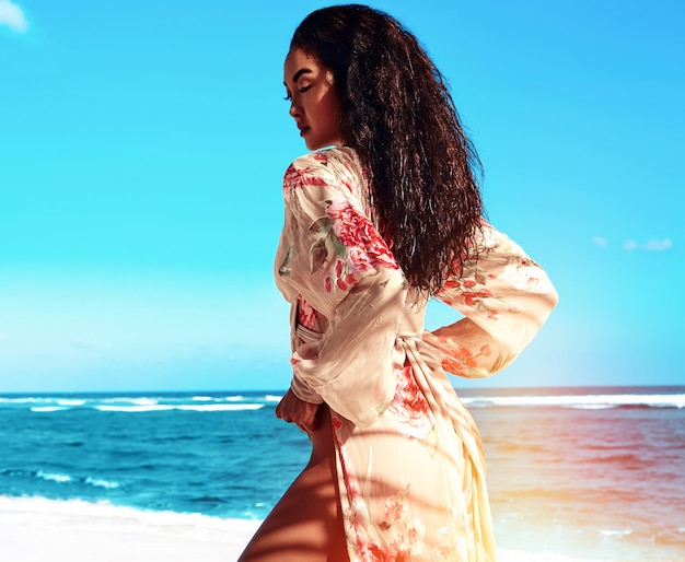 Mulher com cabelo comprido escuro em vestido bege posando na praia de verão