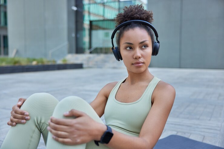 Foto grátis mulher com cabelo encaracolado fortalece o núcleo faz exercícios no colchonete ouve música com fones de ouvido focada na distância ouve música nos fones de ouvido