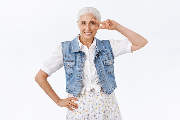 mulher com cabelos grisalhos penteados, mostrando positividade com sinal de paz ou vitória, enviar emoção de boa vontade, sorrindo