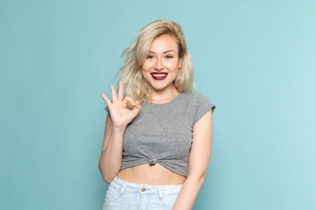 Mulher com camisa cinza e jeans azul brilhante posando com uma expressão feliz e satisfeita