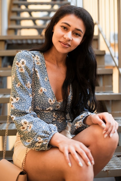 Mulher com camisa floral, sentado na escada e olhando para a câmera