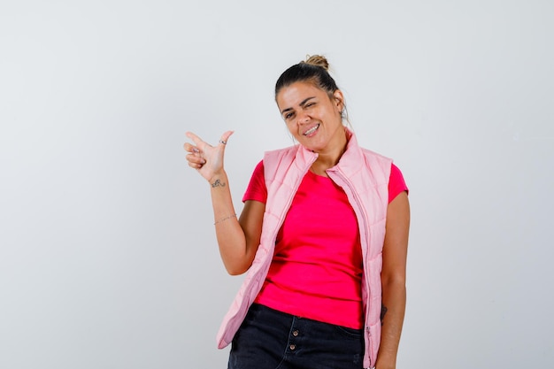 Mulher com camiseta e colete fazendo sinal de pistola com o dedo e parecendo confiante