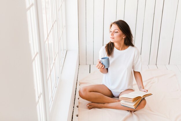 Mulher com caneca e livro, aproveitando a luz do sol