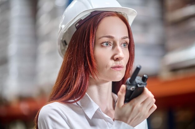Mulher com capacete protetor ouvindo walkie-talkie na mão