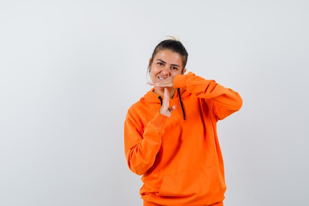 mulher com capuz laranja mostrando gesto de pausa e parecendo alegre