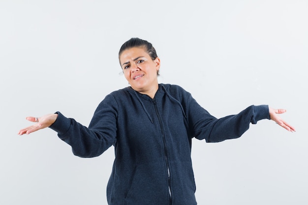 Mulher com capuz, mostrando um gesto desamparado e parecendo confusa, vista frontal.