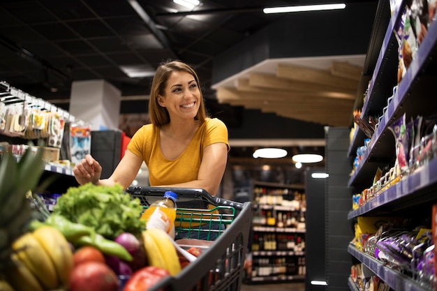 Mulher com carrinho de compras comprando comida no supermercado