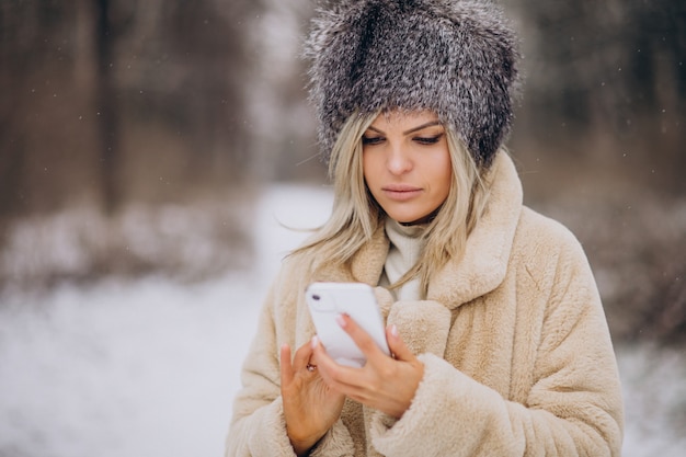 Mulher com casaco de inverno caminhando em um parque cheio de neve falando ao telefone