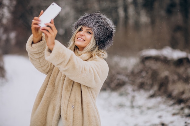 Mulher com casaco de inverno caminhando em um parque cheio de neve falando ao telefone