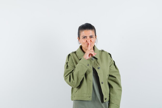 mulher com casaco, t-shirt mostrando gesto de silêncio e parecendo confiante