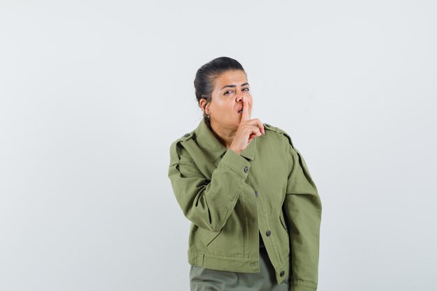 mulher com casaco, t-shirt mostrando gesto de silêncio e parecendo confiante