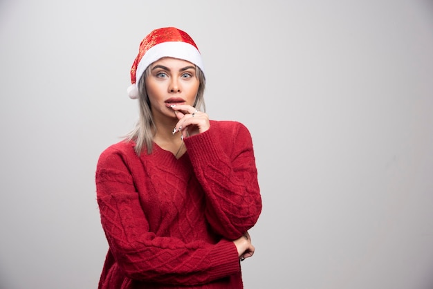 Mulher com chapéu de papai noel pensando intensamente em fundo cinza.