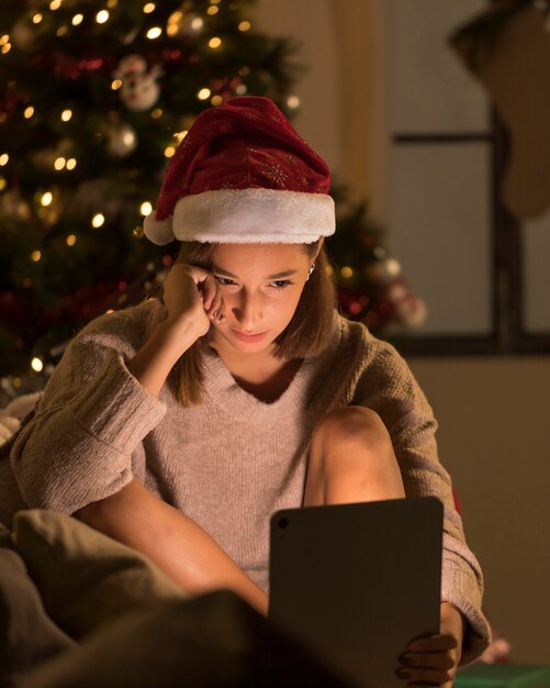 Mulher com chapéu de Papai Noel segurando tablet