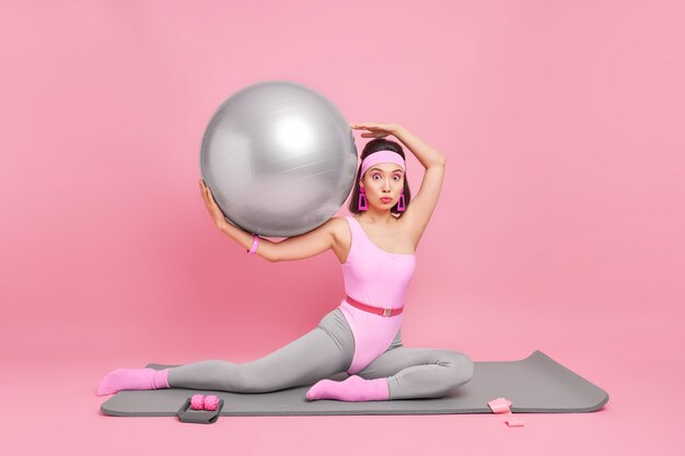 mulher com corpo em forma faz exercícios aeróbicos sendo instrutora de fitness trabalha no centro de treinamento segura bola de pilates vestida com roupas esportivas