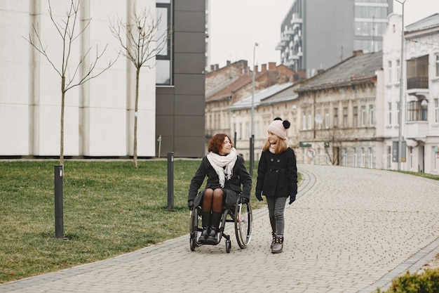 Mulher com deficiência em cadeira de rodas com filha. Família caminhando ao ar livre no parque.