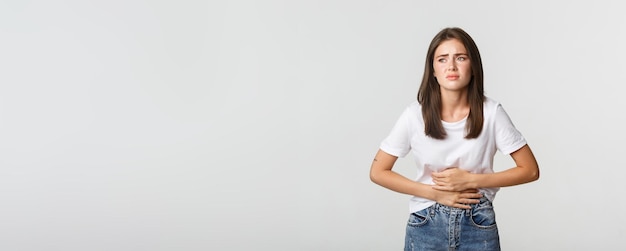 Mulher com dor de estômago dobrando e segurando as mãos no desconforto da barriga de cólicas menstruais